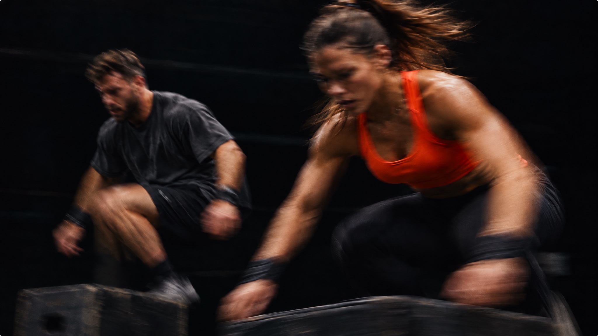 Dos atletas entrenan con cajones, una mujer de naranja y un hombre con camiseta oscura